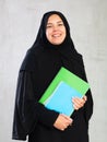 Smiling young female student dressed in traditional islamic clothes holding textbooks