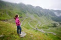 Smiling young female tourist looking far in winding mountain Transfagarashan road in Romania. Royalty Free Stock Photo