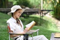 Smiling young female traveler resting on folding chair and reading book. Adventure, travel, tourism and camping concept Royalty Free Stock Photo