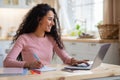 Smiling Young Freelancer Woman Working With Laptop In Kitchen And Taking Notes Royalty Free Stock Photo