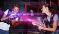 Smiling young friends playing laser tag game with colored laser