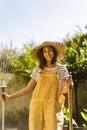 Smiling young gardener with straw hat with rake and shovel in her hands. Gardening.