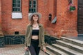 A smiling young girl with blond long hair, in black leggings, a tank top, a beige jacket and a hat Royalty Free Stock Photo