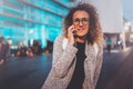 Smiling young girl calling with her cell telephone while standing at night on the street. Bokeh and flares effect on