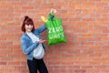 Smiling young girl demonstrates a green textile eco bag with white text zero waste on a brick wall background.