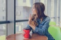 Smiling young girl in jeans shirt drinking coffee, sitting in a cafe and waving to her friend. Takeaway shop to-go coffee. Waiting Royalty Free Stock Photo