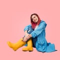Smiling young girl sits on floor wearing spring raincoat protected from the rain and tall yellow rubber boots. Royalty Free Stock Photo