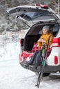 Smiling young girl skier sitting inbuilt compartment for luggage of car and drinking hot tea from cup. Winter wood Royalty Free Stock Photo