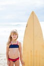 Smiling young girl standing next to surfboard Royalty Free Stock Photo