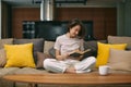 Smiling young girl student reading paper book rest sitting on sofa in living room at home enjoy novel. Self education Royalty Free Stock Photo