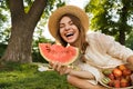 Smiling young girl in summer hat having a picnic at the park, sitting on a grass Royalty Free Stock Photo