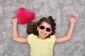 Young girl with sunglasses and red plush heart lying on the carpet Royalty Free Stock Photo