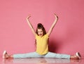 Smiling young girl or teen girl in jeans and yellow t-shirt does the splits and holds hands up