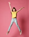Smiling young girl or teen girl in jeans and yellow t-shirt have fun jumping high with her arms and legs spread