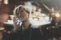 Smiling young girl using smartphone on background glow bokeh light in night atmospheric city.Hipster girl using in hands