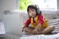 Smiling young girl wearing headphones uses laptop sitting on the sofa Royalty Free Stock Photo