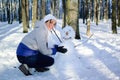 Smiling young girl in white hat and scarf hugging funny snowman in the park during a sunny day. Blue sky and frosty Royalty Free Stock Photo