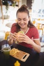 Smiling young gorgeous woman eating burger at coffee shop Royalty Free Stock Photo