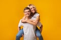 Smiling young guy carrying girlfriend on his back