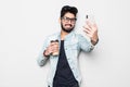 Smiling young guy taking selfie photo on smartphone with coffee cup in hands . Indian man using digital device. Selfie photo Royalty Free Stock Photo