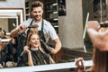 Smiling young hairstylist combing and drying hair to happy young woman