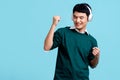 Smiling young handsome asian man listening to the music on cellphone using earbuds, He is dancing isolated in blue background Royalty Free Stock Photo