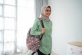 Smiling young hijab traveler carrying her bag and holding suitcase