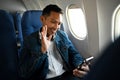 Smiling young hipster male passengers using smart phone having video call on mobile phone while sitting on aircraft Royalty Free Stock Photo