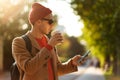 Smiling hipster man wear sunglasses using cellphone standing at the street drinking takeaway coffee Royalty Free Stock Photo