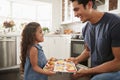 Smiling young Hispanic girl standing in kitchen presenting the cakes she has baked to her father