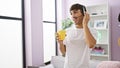 Smiling young hispanic man happily teleworking at home - agent for a call center, hands-free call gadget on, savoring coffee in Royalty Free Stock Photo