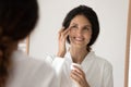 Smiling young hispanic woman apply nourishing cream under eyes Royalty Free Stock Photo