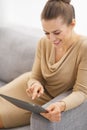 Smiling young housewife sitting on couch and using tablet pc Royalty Free Stock Photo