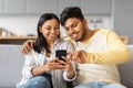 Smiling Young Indian Couple Using Smartphone And Embracing Together At Home Royalty Free Stock Photo