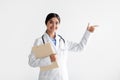 Smiling young indian lady in white coat with tablet shows finger at empty space, isolated on white background