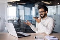 A smiling young Indian man is working in the office using a laptop, sitting at a desk and talking on the phone in a Royalty Free Stock Photo