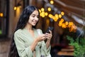 A smiling young Indian woman in a green suit stands on an evening city street and uses a mobile phone in her hands and Royalty Free Stock Photo