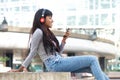 Smiling young Indian woman sitting outside in the city listening to music with smart phone and headphones Royalty Free Stock Photo