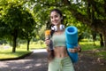 Indian woman in tracksuit with yoga mat and water bottle enjoying fitness in park Royalty Free Stock Photo