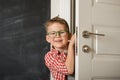 Smiling young kid boy peeking out of door. School kid come back from school. Happy child in glasses. Hand on handle