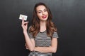 Smiling young lady over grey wall holding debit card