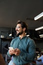 Smiling young Latin business man holding mobile phone standing in office. Royalty Free Stock Photo
