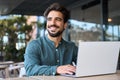 Smiling young Latin business man using laptop working outdoors looking away. Royalty Free Stock Photo