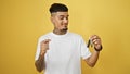 Smiling young latin man confidently pointing to key of his new car, isolated on yellow background Royalty Free Stock Photo