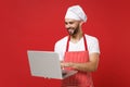 Smiling young male bearded chef cook or baker man in striped apron t-shirt toque chefs hat isolated on red background Royalty Free Stock Photo