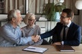 Smiling young male broker handshaking with old age family couple Royalty Free Stock Photo
