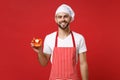 Smiling young male chef cook or baker man in striped apron white t-shirt toque chefs hat isolated on red background Royalty Free Stock Photo