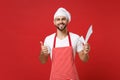 Smiling young male chef cook or baker man in striped apron white t-shirt toque chefs hat isolated on red wall background Royalty Free Stock Photo