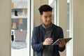Smiling young male freelancer using digital tablet, standing in bright modern home office Royalty Free Stock Photo