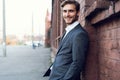 Smiling young male manager formal dressed leaning on a wall outdoors. Royalty Free Stock Photo